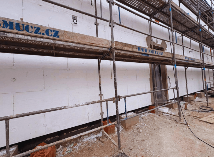 Průběh kompletní realizace a zateplení fasády o ploše 1000 $m^2$ v Blansku od firmy Misterstav. Fotografie detailně zachycují pokládku polystyrenu, armování perlinkou kolem oken a aplikaci finální moderní šedé omítky.