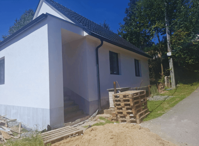 Komplexní rekonstrukce rodinného domu v Židlochovicích od firmy Misterstav. Fotografie zachycují výměnu sedlové střechy za novou skládanou krytinu, pokládku izolace a svařování PVC fólie na ploché terase a realizaci nové zateplené bílé fasády.